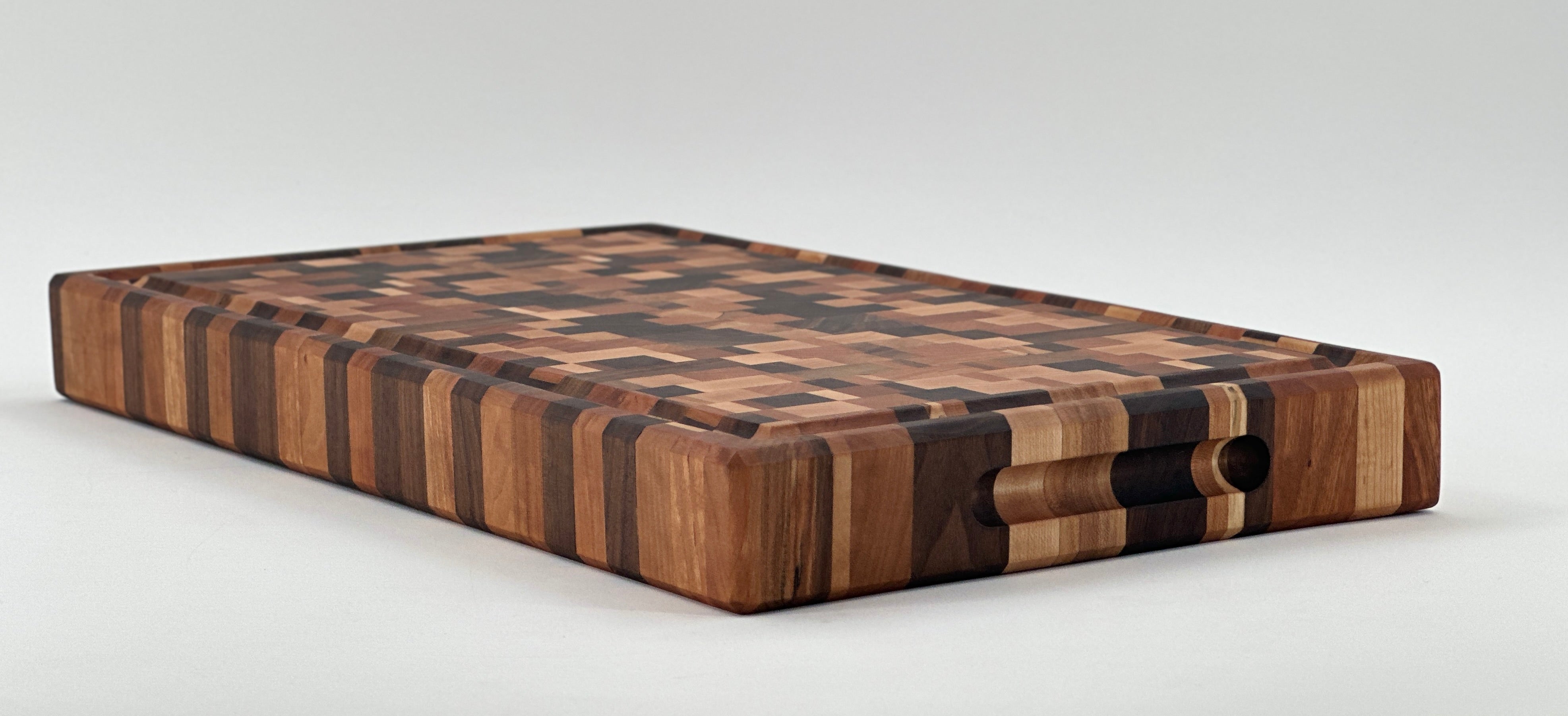 End grain cutting block made of cherry, maple, and walnut hardwoods with juice groove and indented handgrips